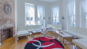 A spacious living room with a brick fireplace, white sofas, a coffee table, and large windows with sheer curtains. - JGSTAY - Koreatown (New York)