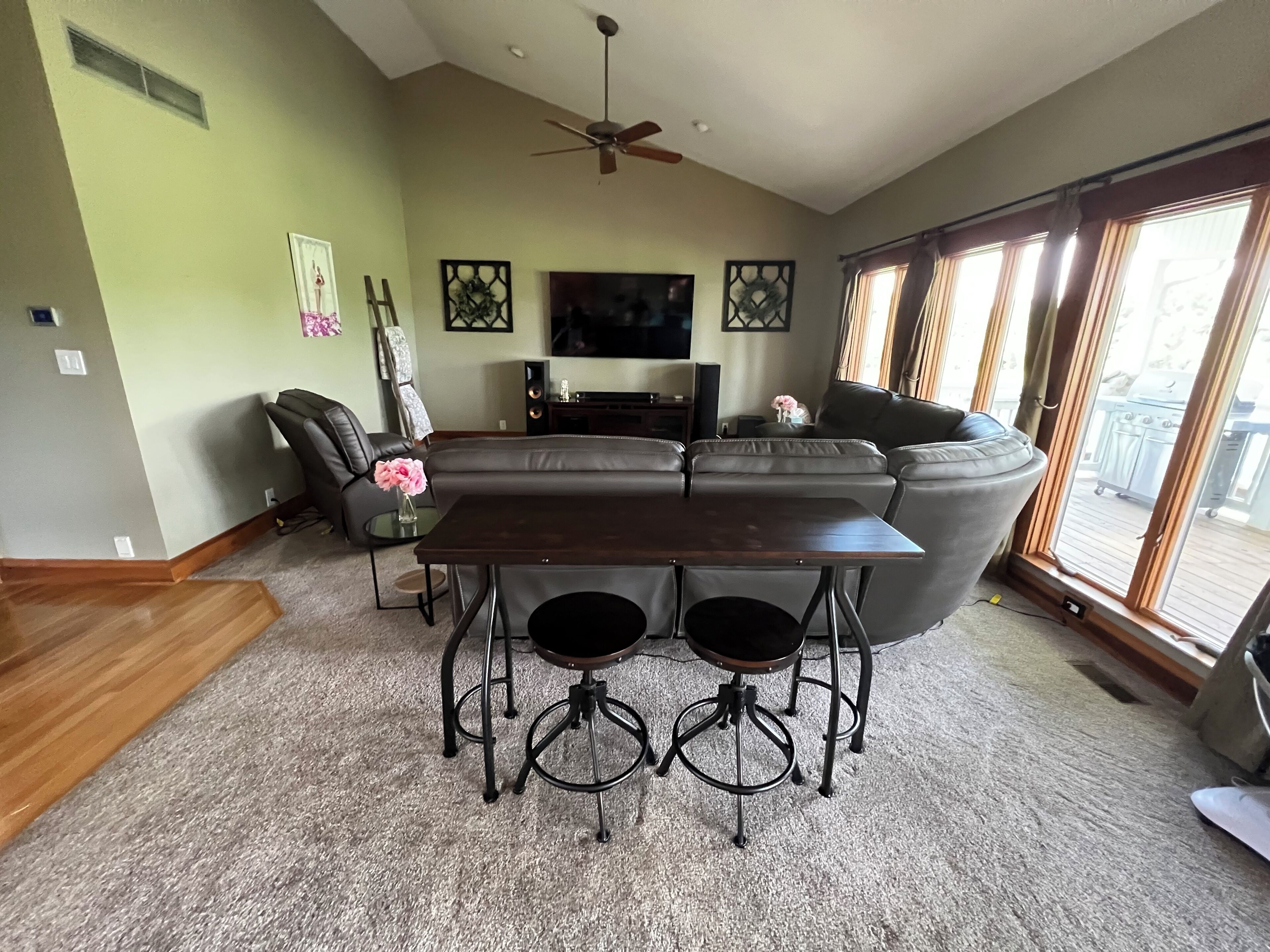 A living room with a sectional sofa, a dark wooden coffee table, and a TV on the wall.