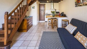 Ein gemütliches Wohnzimmer mit einer dunklen Couch, einem gemusterten Teppich, einer Holztreppe und einer Küchenzeile mit Mikrowelle und Barhocker.