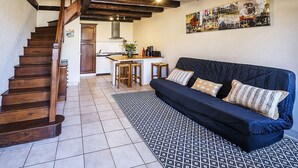 Ein gemütlicher Wohnbereich mit einem dunkelblauen Sofa, einer Holztreppe, einem gefliesten Boden und einer Küche im Hintergrund.