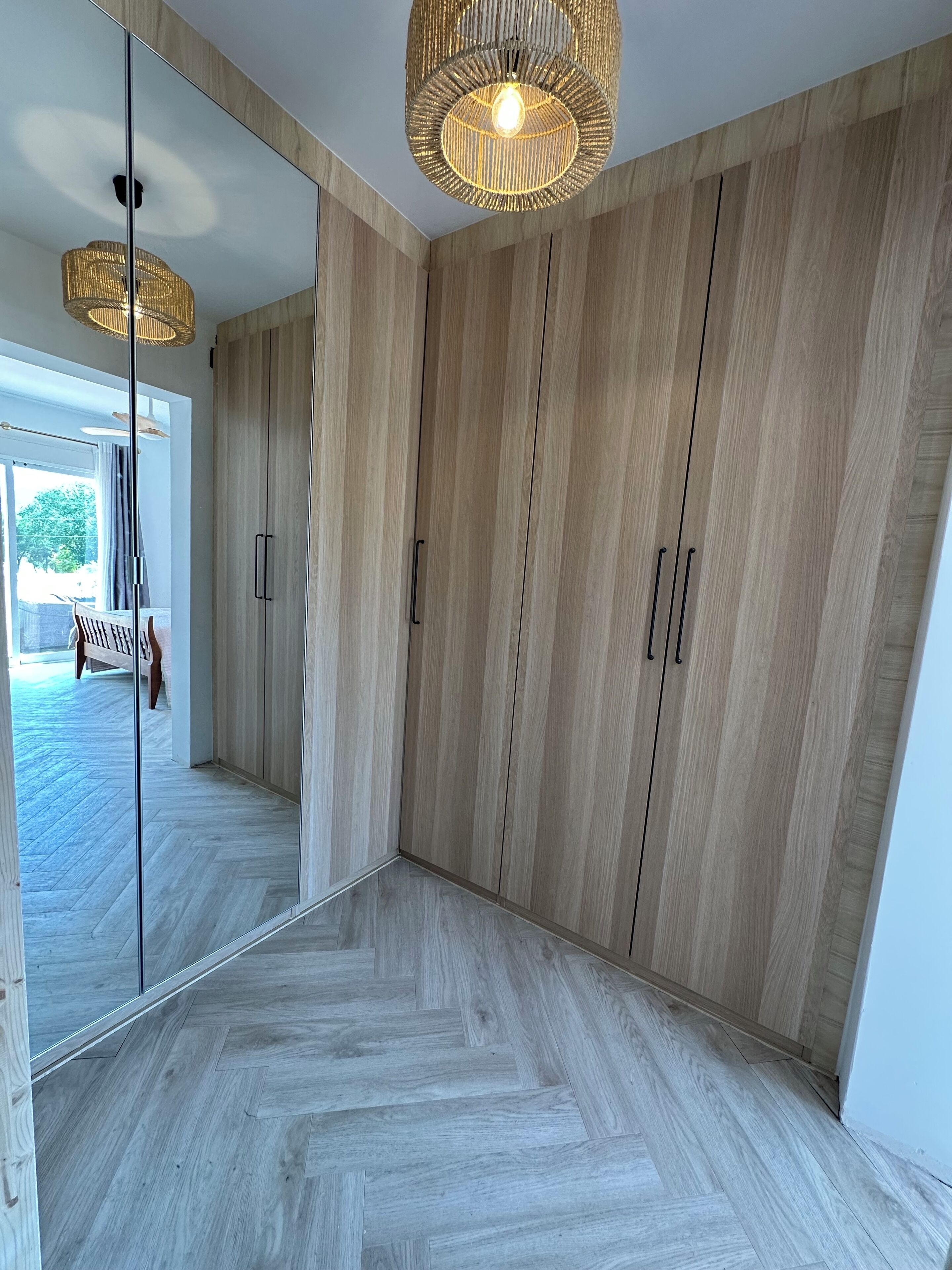 A modern room with wooden flooring, a large mirror, and a hanging light fixture.