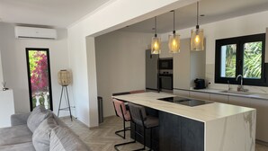 Une cuisine moderne dotée d’un îlot central, de luminaires suspendus et offrant une vue sur la verdure environnante.