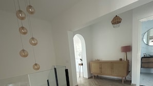 Une pièce spacieuse dotée d’un parquet en bois à motifs en chevrons, d’une rambarde en verre, d’un meuble en rotin et d’un luminaire suspendu.