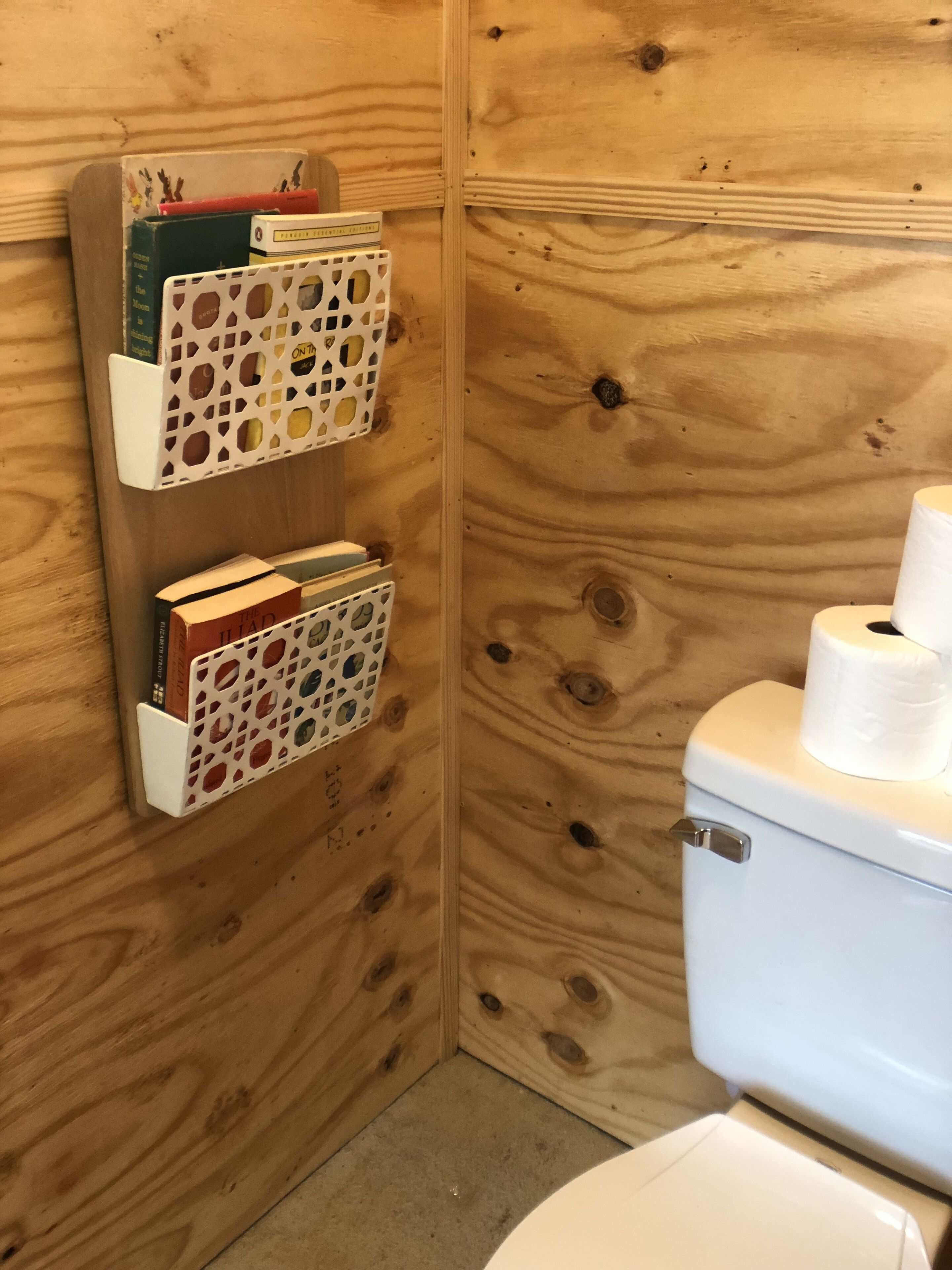 A wooden bathroom with two white storage units with circular cutouts, a toilet, and a roll of toilet paper on the right.