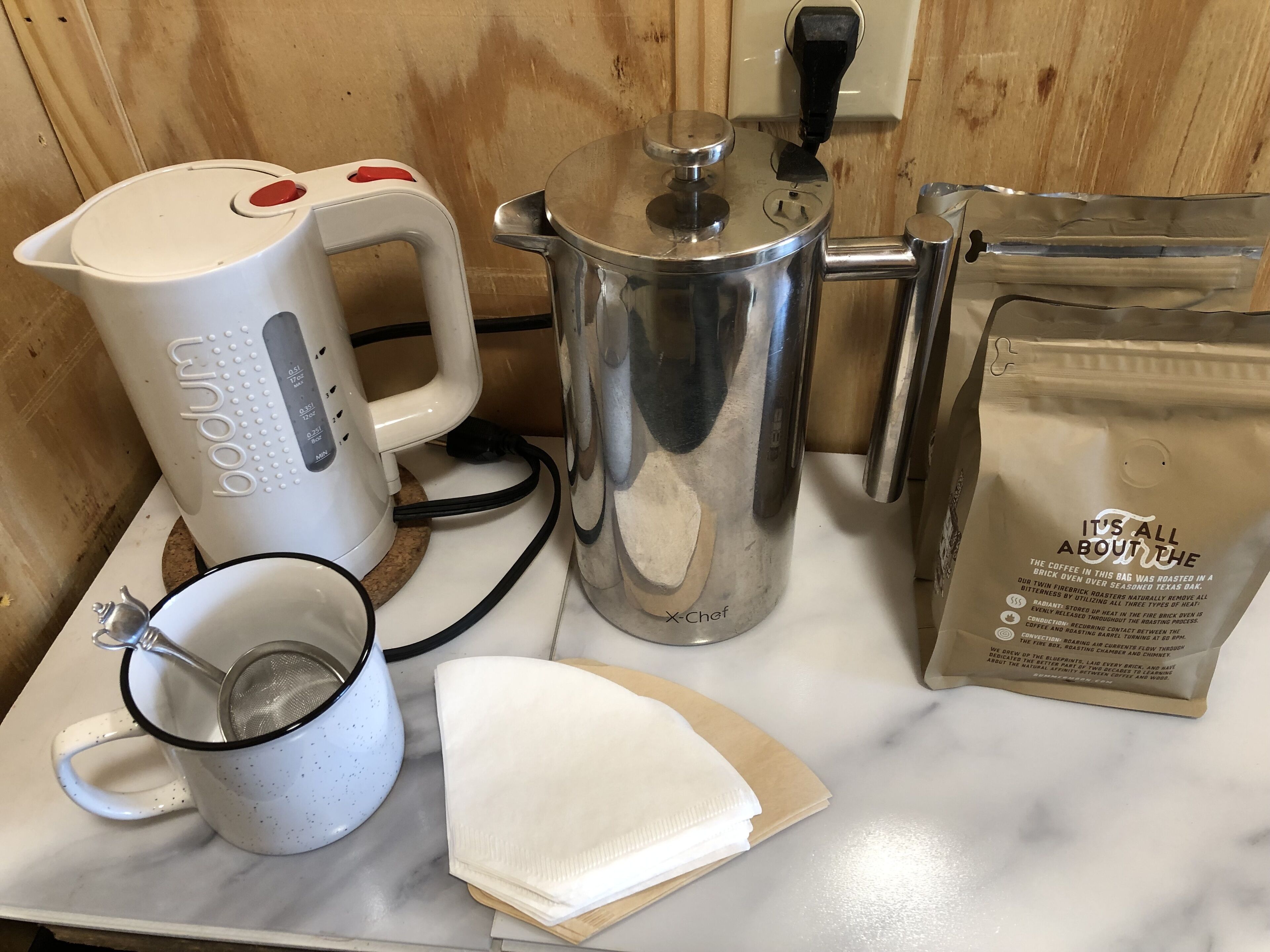 A kitchen counter with a coffee maker, a pot, a bag of coffee, a mug, and a strainer.