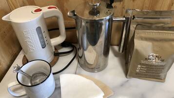A kitchen counter with a coffee maker, a pot, a bag of coffee, a mug, and a strainer.