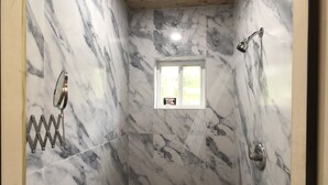 Un baño con paredes de mármol, ducha, ventana y perchero.