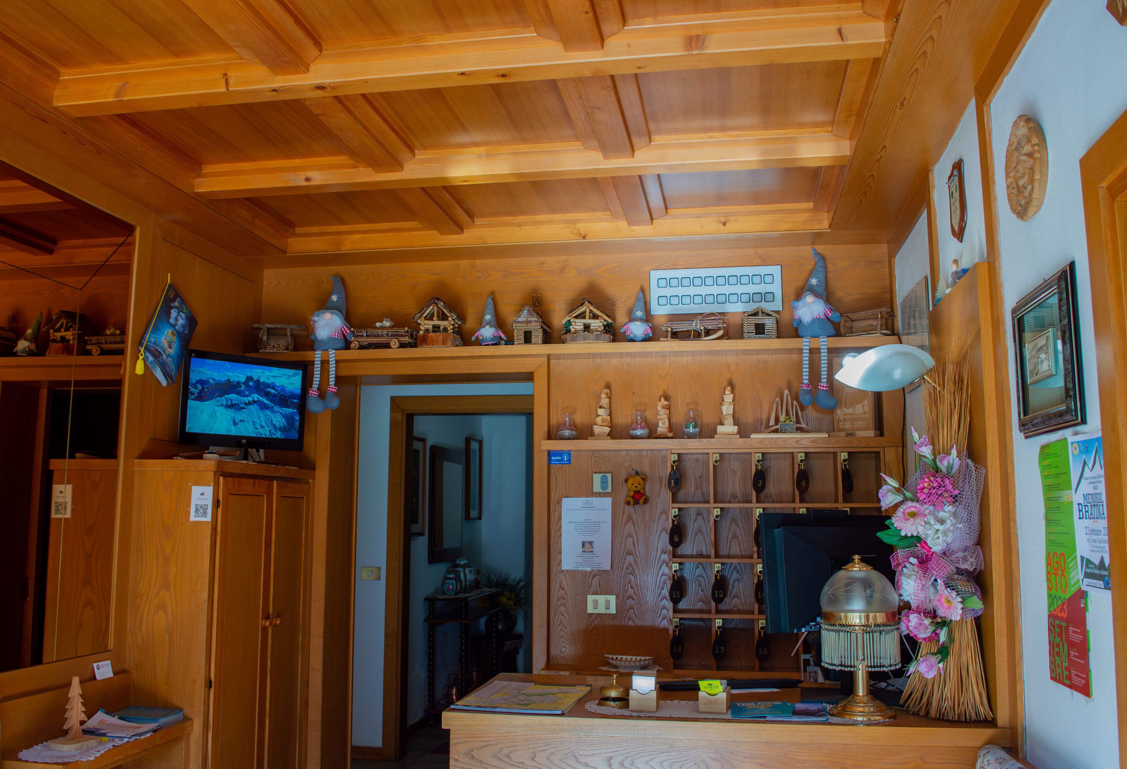 A wooden interior with a television, shelves with decorative items, a desk with a lamp, and a broom.