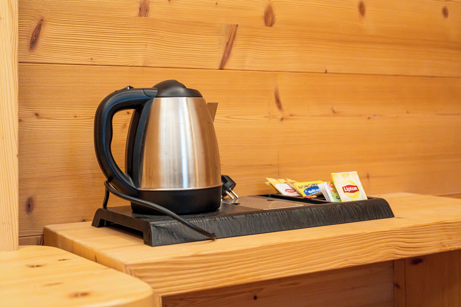A stainless steel kettle on a wooden table with a wooden wall background.