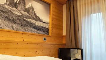 A hotel room with wooden walls, a bed with a white comforter, a black-framed television, and a large mountain landscape painting.