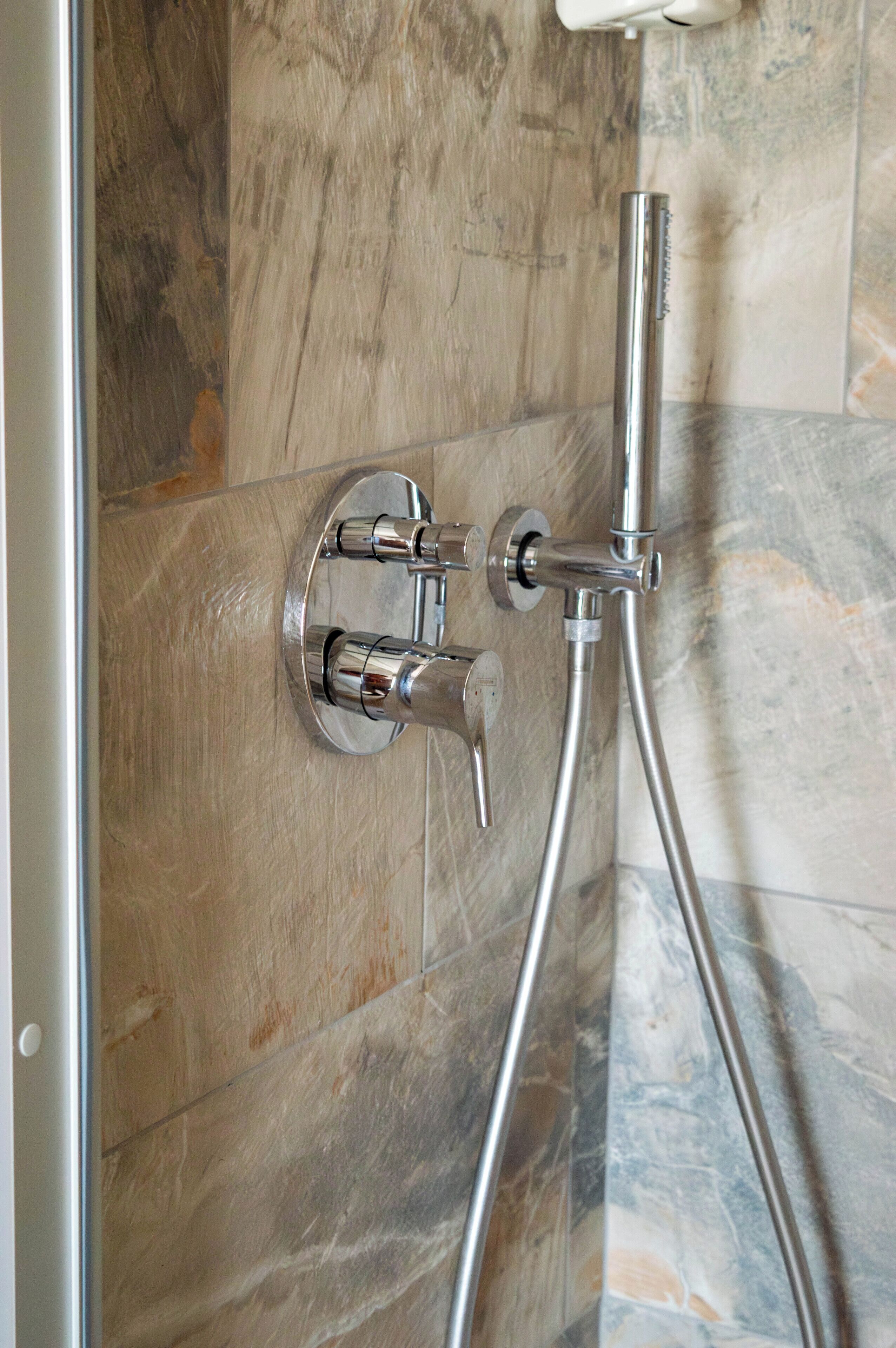 Une douche dotée d’un panneau de commande fixé au mur et d’un pommeau de douche à main.