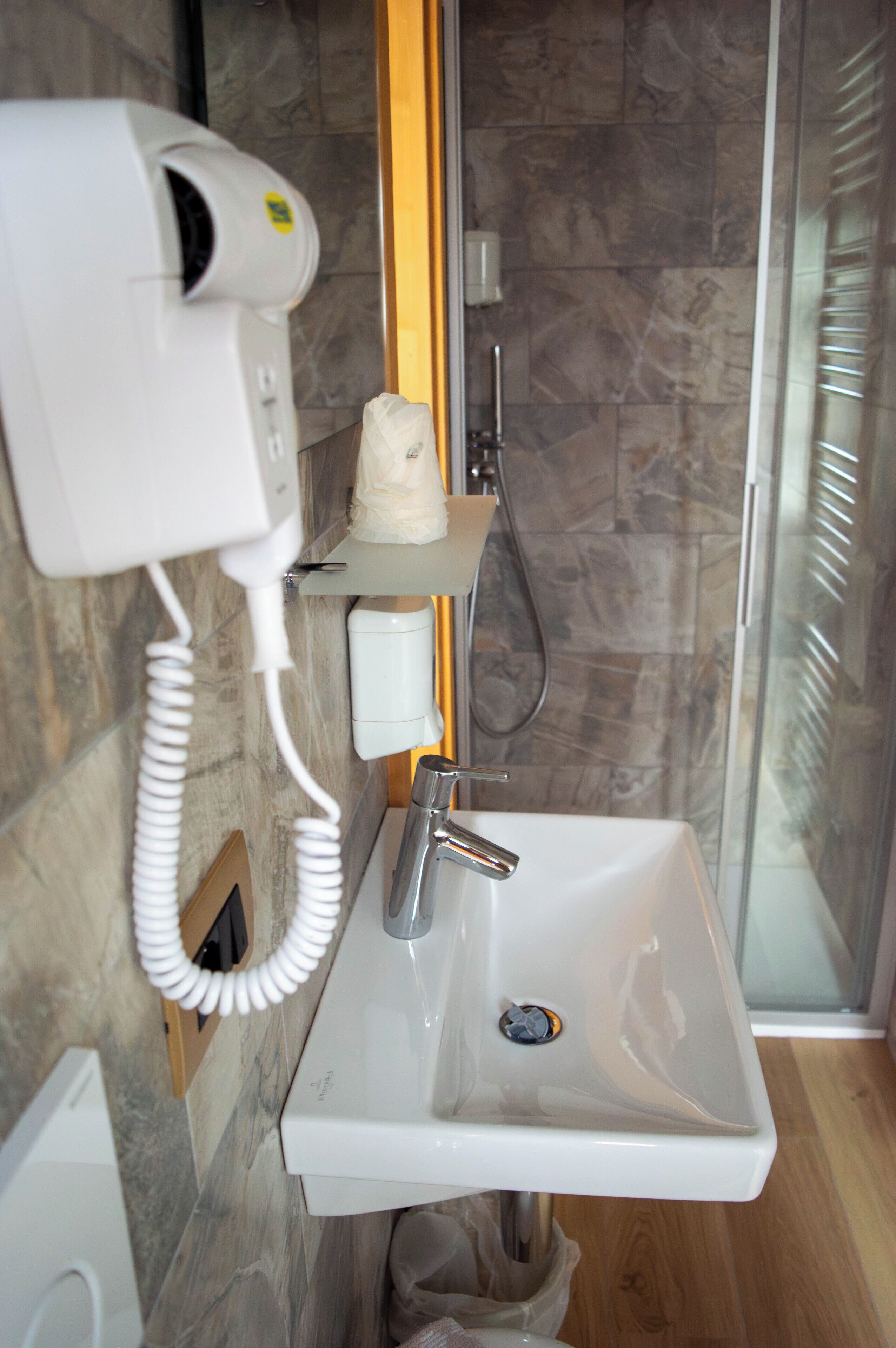 Un baño con lavamanos blanco, secador de pelo de mano y ducha.