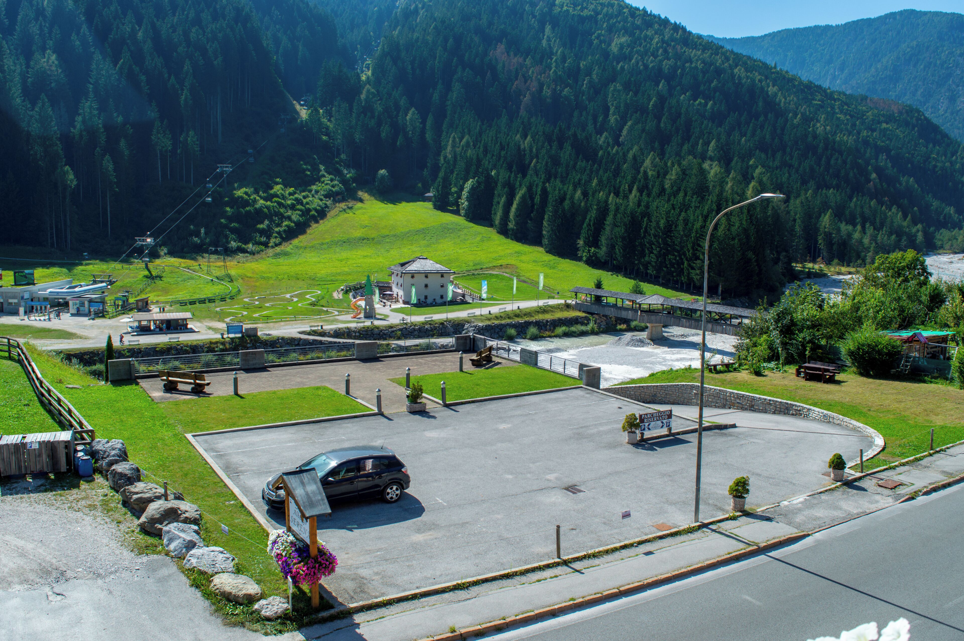 Uma área de estacionamento com um carro, um edifício com telhado verde e montanhas ao fundo.