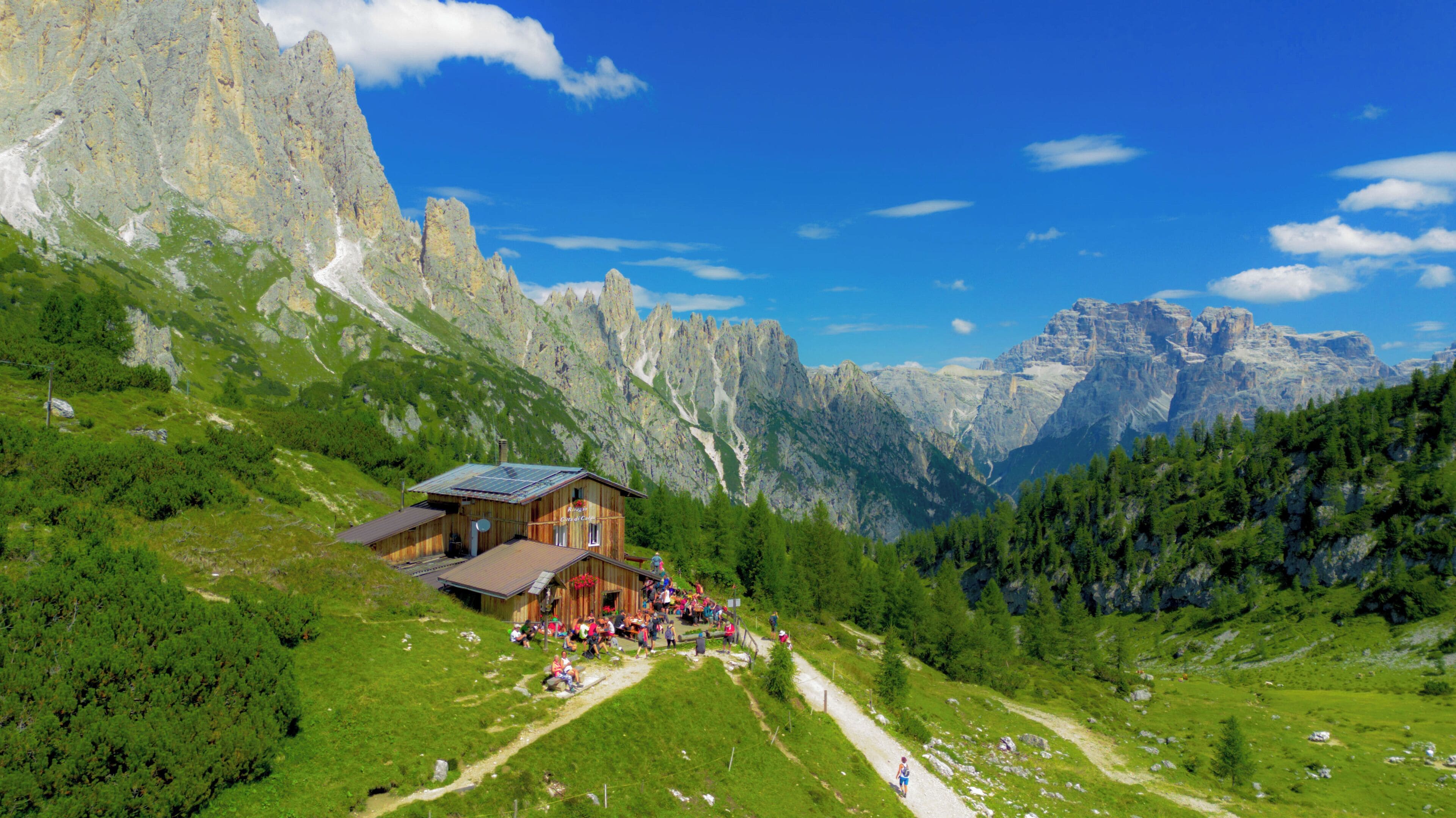 A mountain lodge with a wooden exterior, a solar panel roof, and a scenic view of towering mountains.