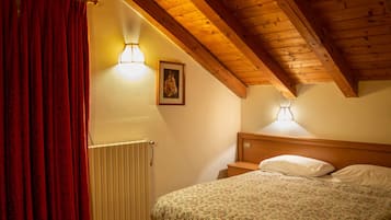 A bedroom with a wooden ceiling, a radiator, a bed with a floral bedspread, and two wall-mounted lamps.