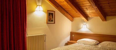 A bedroom with a wooden ceiling, a radiator, a bed with a floral bedspread, and two wall-mounted lamps.