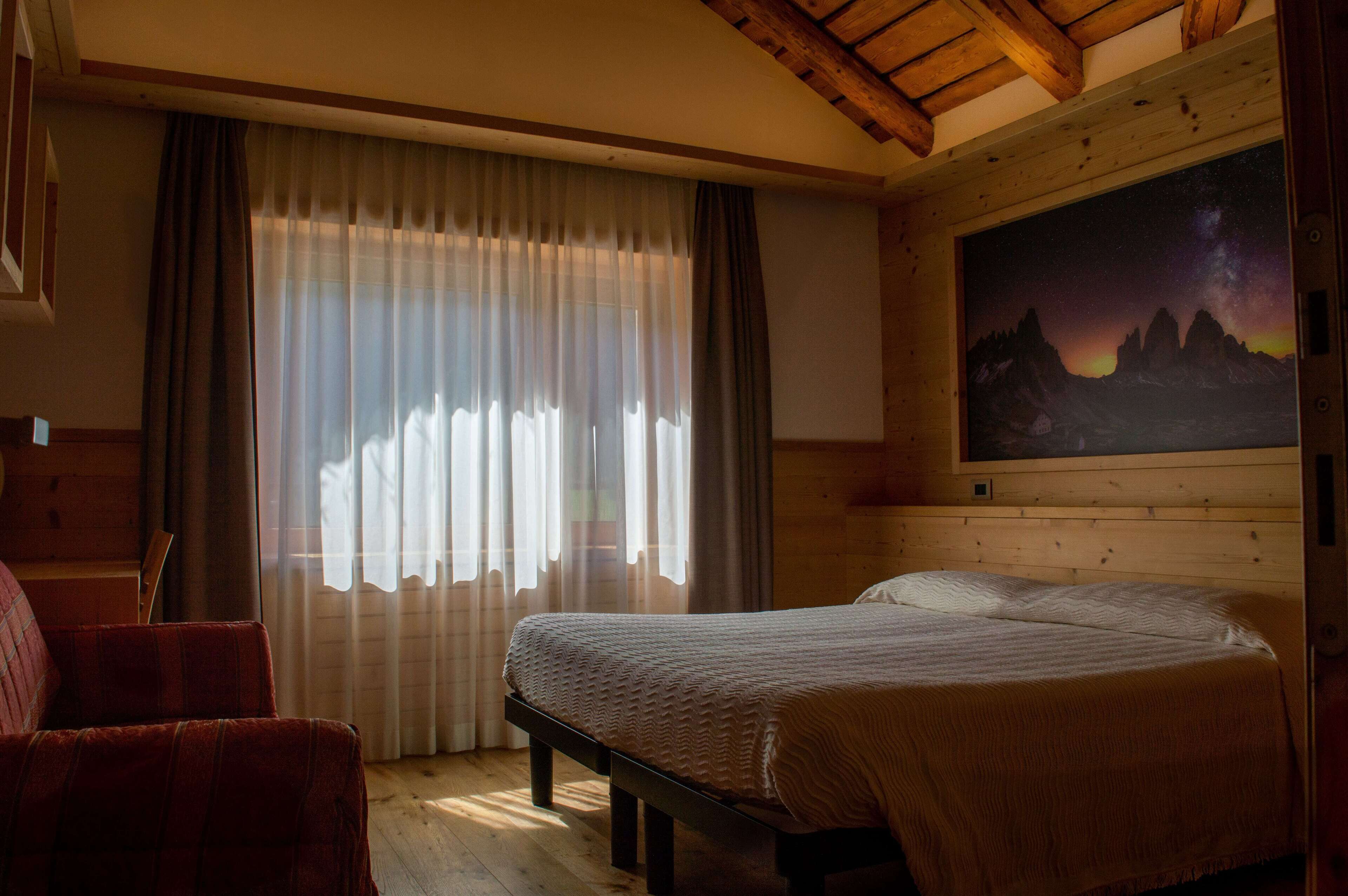 A bedroom with a bed, a chair, a painting of mountains, and wooden walls.