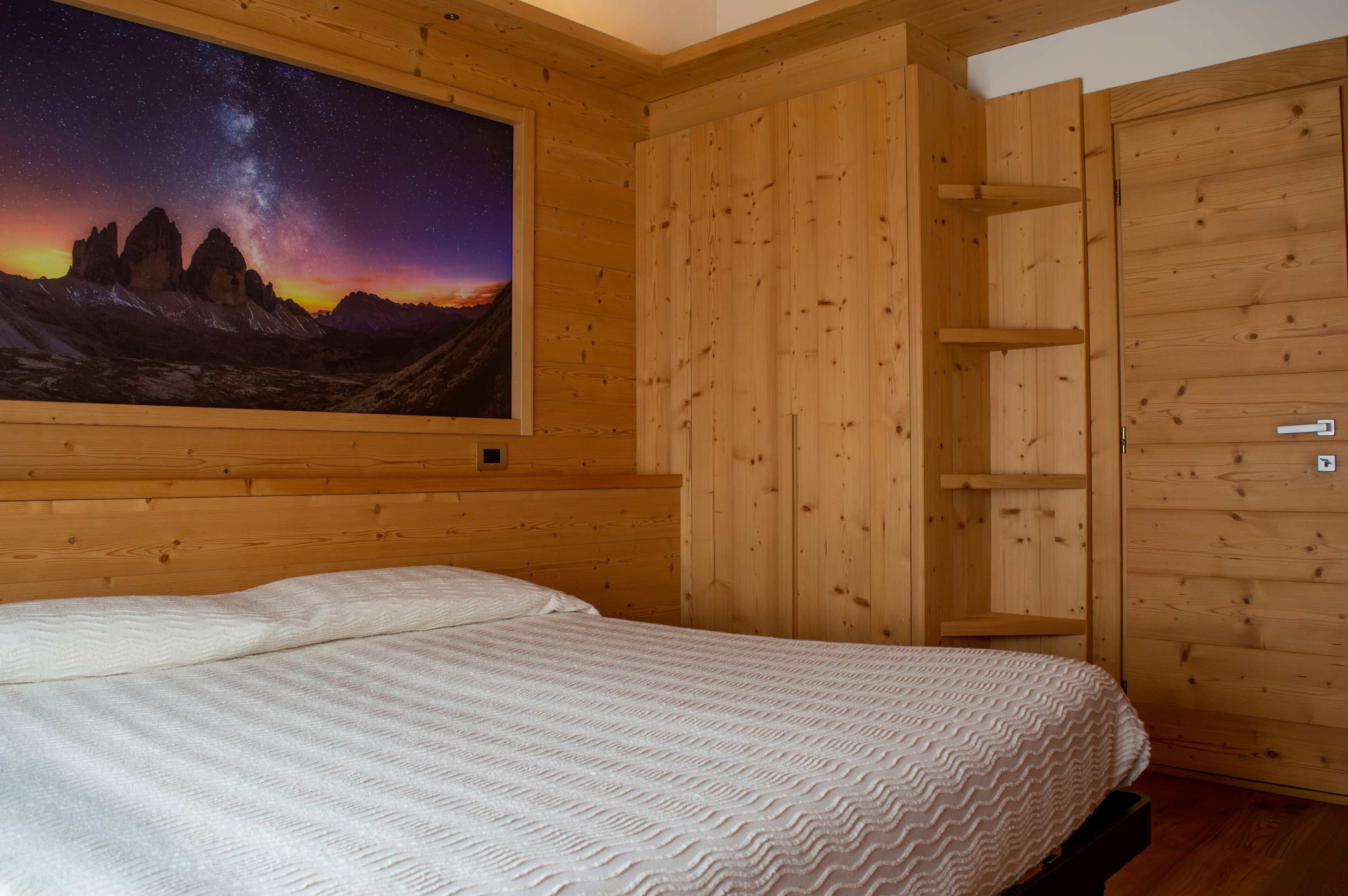A bedroom with a bed, wooden walls, a starry night mural, and a wooden wardrobe.