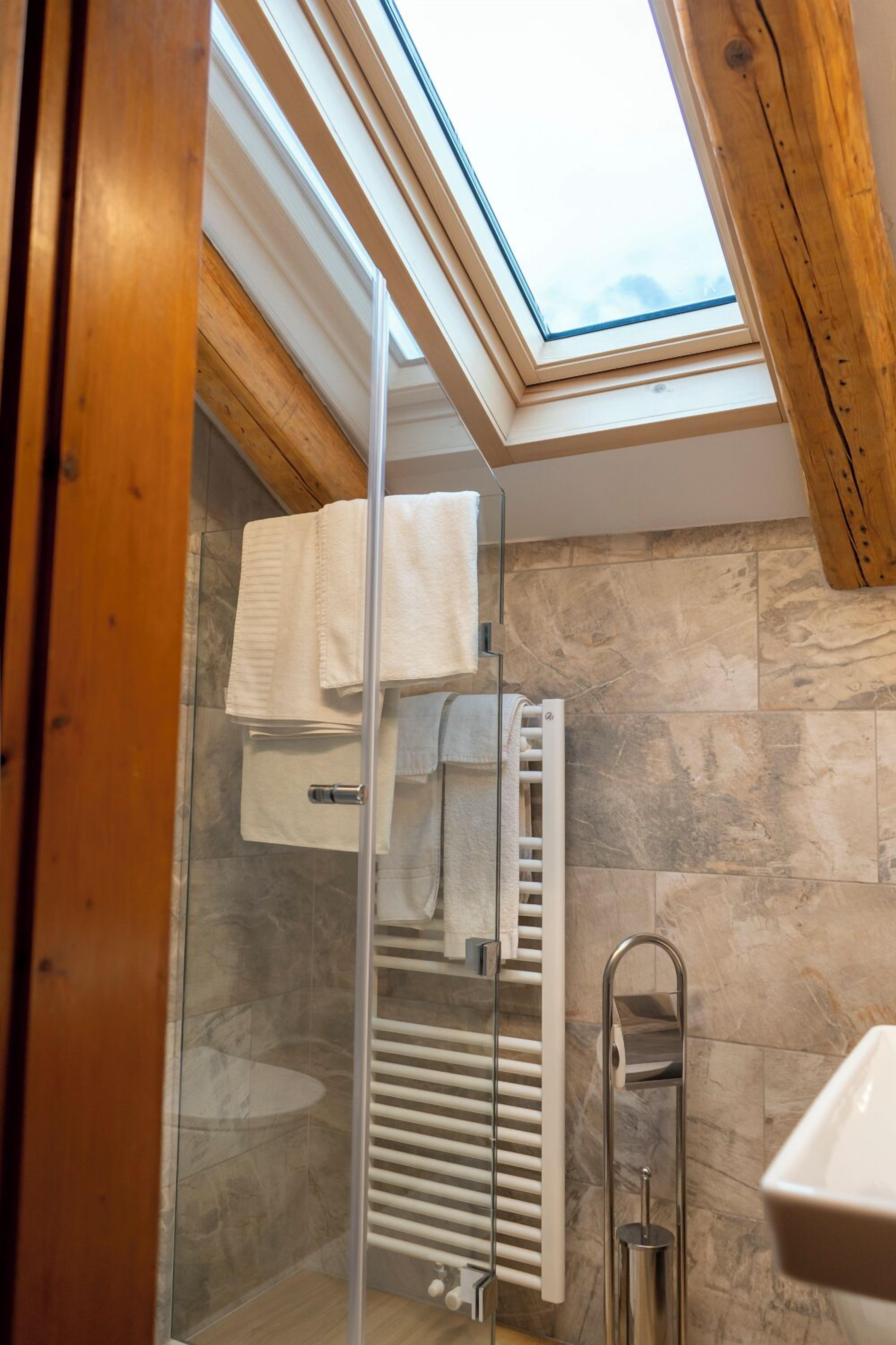 A modern bathroom with a skylight, a glass shower enclosure, a white sink, and a towel rack.