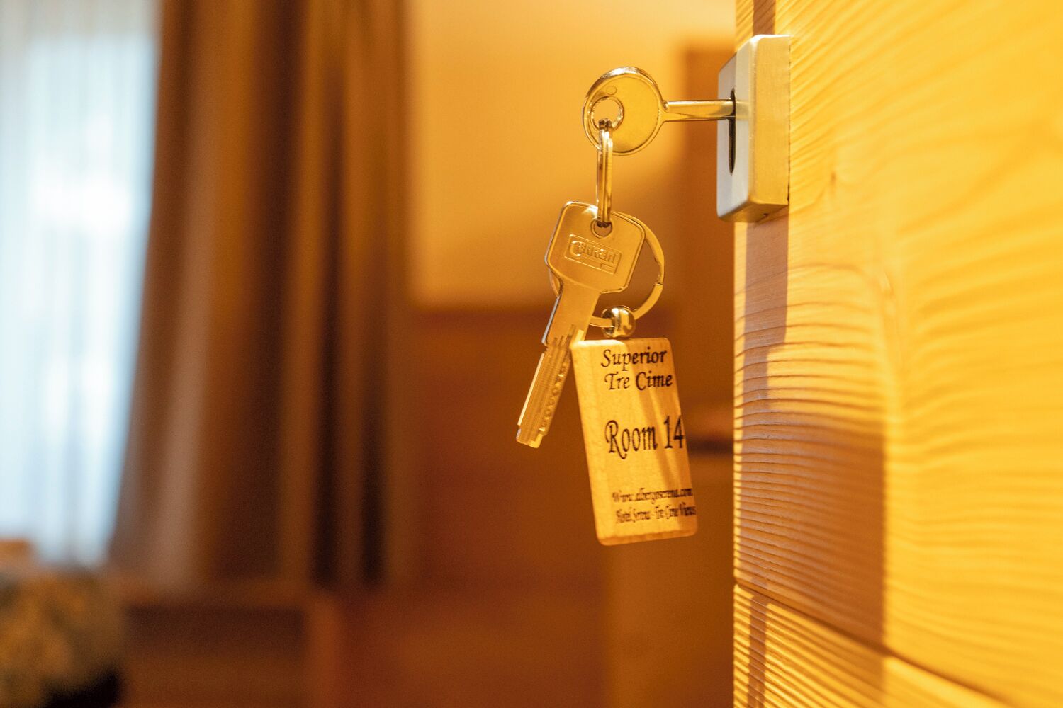 Un porte-clés avec une étiquette indiquant « Chambre 14, catégorie supérieure, Tre Cime », attaché à une poignée de porte.