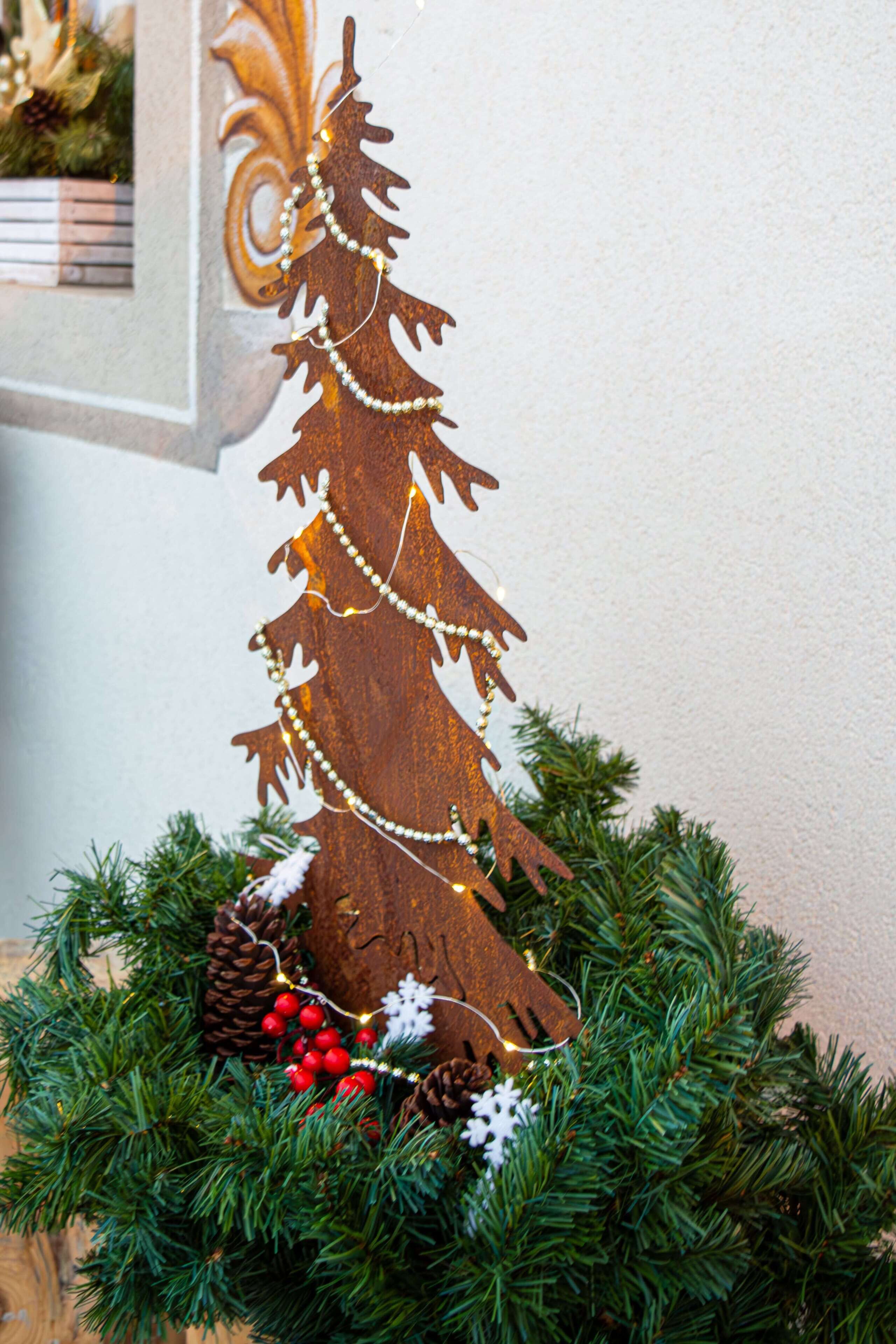 Un árbol de Navidad de madera con luces y adornos, rodeado de ramas y piñones de pino.