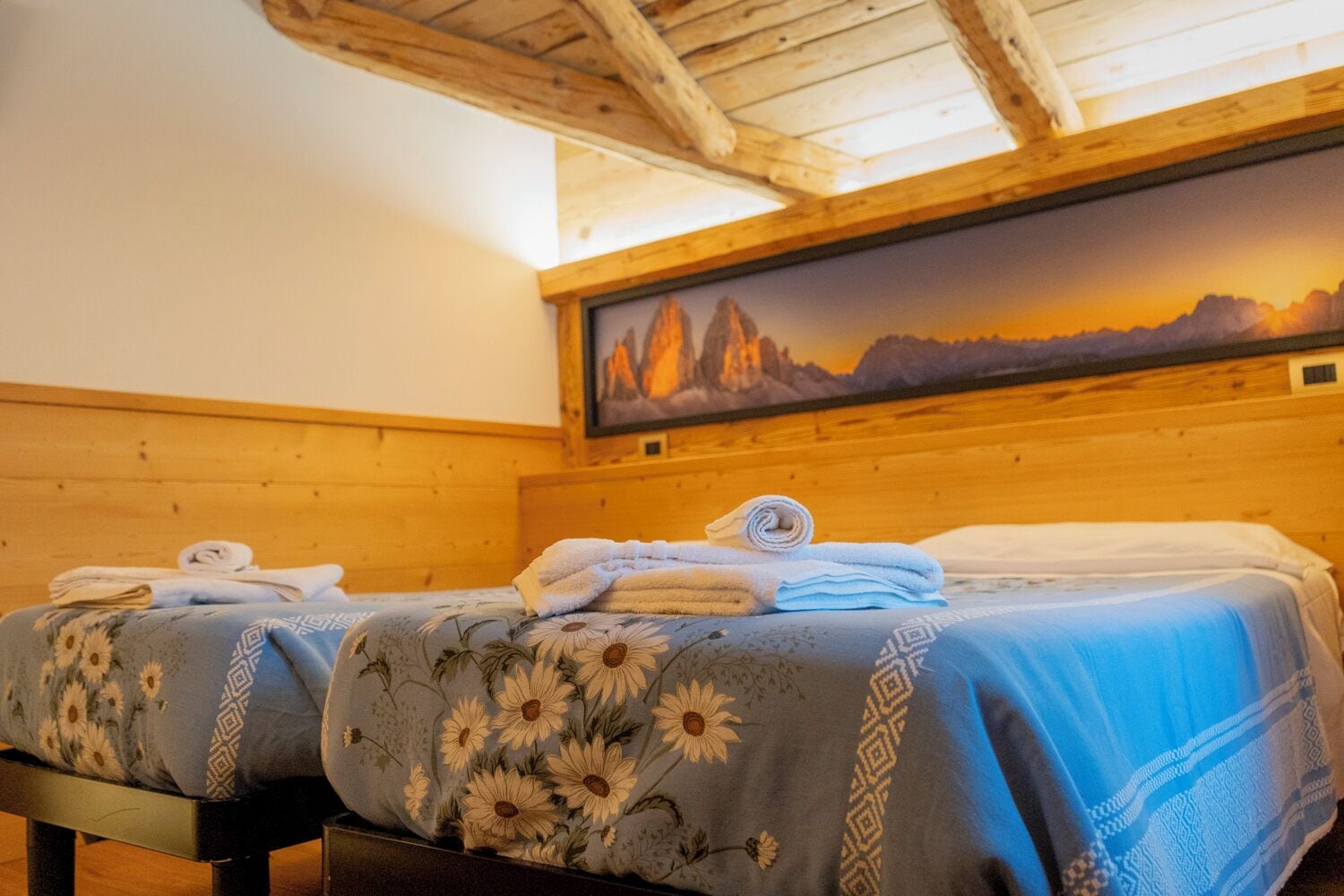 Una habitación con dos camas, vigas de madera en el techo y un cuadro de un paisaje montañoso.
