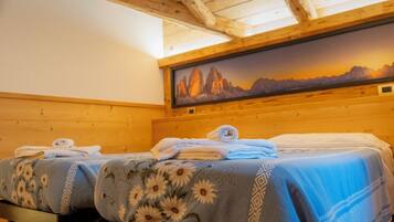 Una habitación con dos camas, vigas de madera en el techo y un cuadro de un paisaje montañoso.