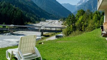 A chair on a grassy area with a view of a river and mountains.