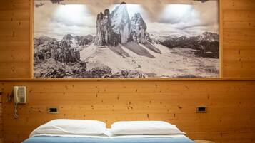 Quarto de hotel com cama, paredes de madeira, um quadro pendurado de paisagem montanhosa e um telefone na parede.