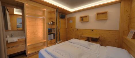 Una habitación de madera con una cama, un escritorio, una silla, un espejo y una repisa con una tetera.