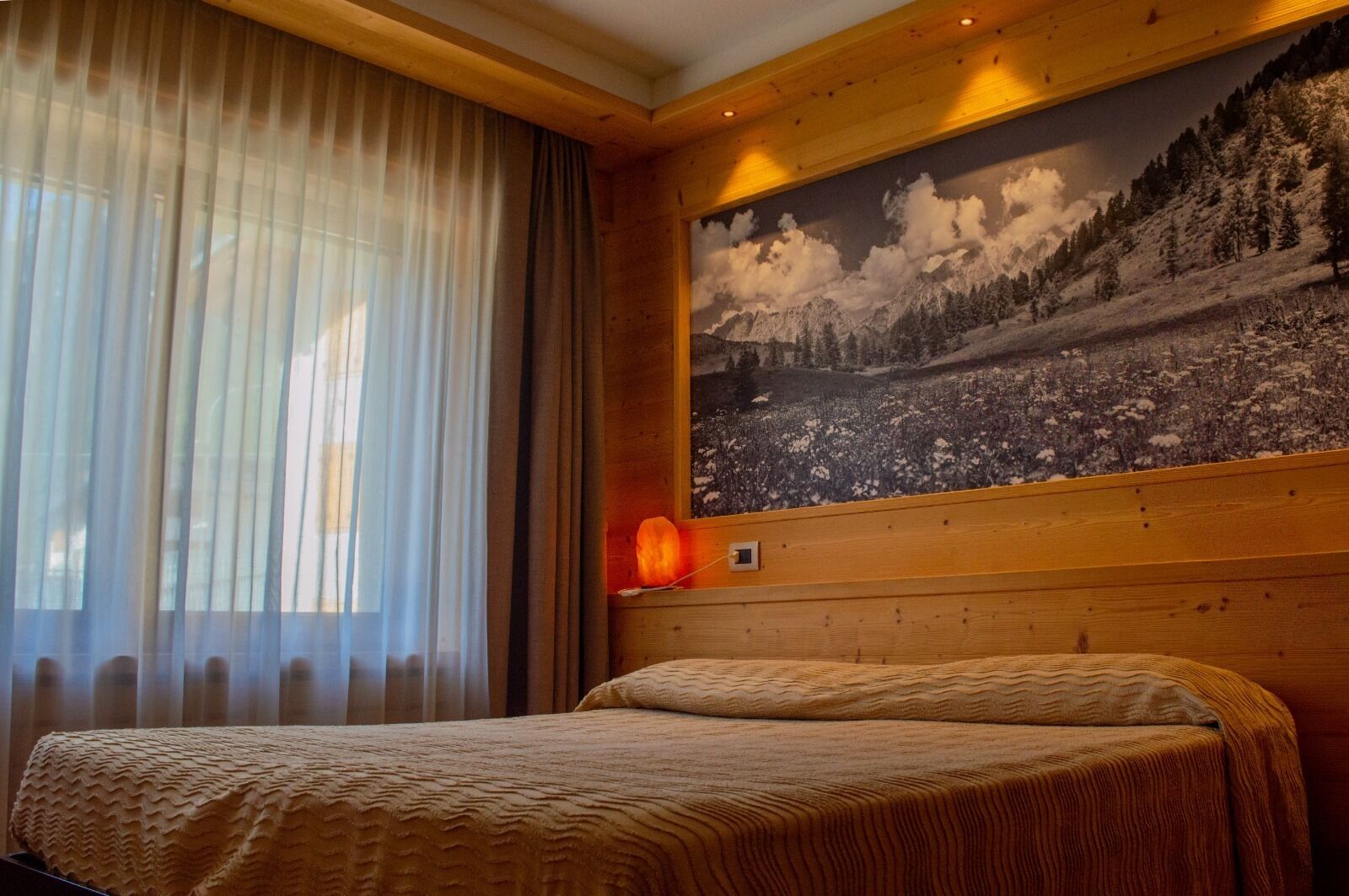 Une chambre à coucher avec un lit, une grande fenêtre avec des rideaux légers et un radiateur fixé au mur.