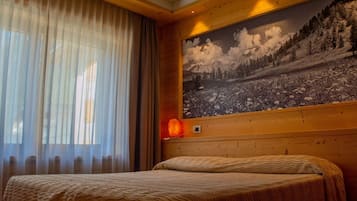 A bedroom with a bed, a large window with sheer curtains, and a wall-mounted heater.