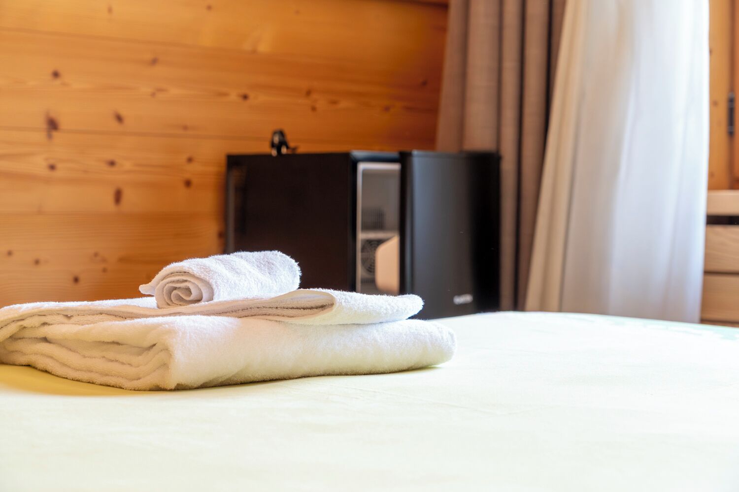 Un letto rifatto con asciugamani piegati e un mobile nero in una stanza in legno.