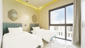 A modern bedroom with two beds, a large window, and a city view. - A modern luxurious 3 bedroom VILLA For family Gatherings, and Buiness meetings (AKOYA 2 - Damac Hills)