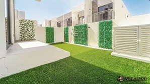 A modern building with a flat roof, white exterior walls, and a green artificial lawn. - A modern luxurious 3 bedroom VILLA For family Gatherings, and Buiness meetings (AKOYA 2 - Damac Hills)