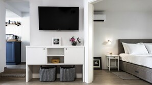 A modern hotel room with a flat-screen TV mounted on the wall, a bed with white linens, a small bedside table with a lamp, and a grey sofa. - Charming seaside house with home office (Pag)