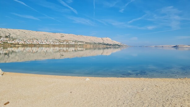 A calm lake with a clear sky, a sandy shore, and a distant mountain range. - Charming seaside house with home office (Pag)