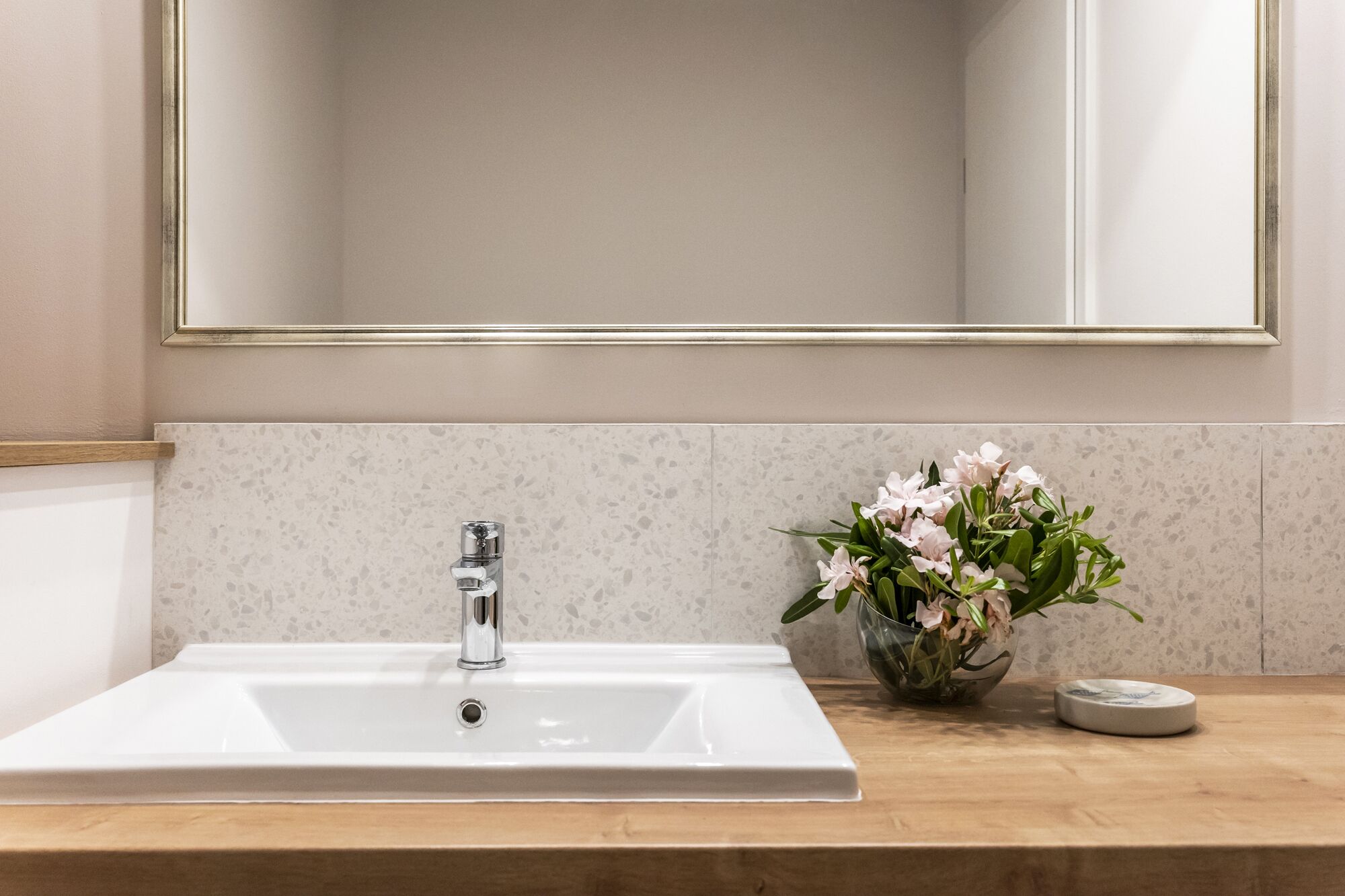 A bathroom with a white sink, a mirror with a gold frame, and a vase with flowers on the countertop.