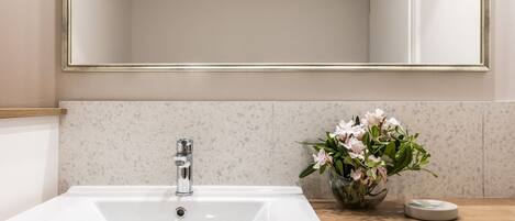 A bathroom with a white sink, a mirror with a gold frame, and a vase with flowers on the countertop.
