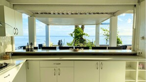 Une cuisine avec des meubles blancs, une cuisinière à gaz et une vue sur la mer.