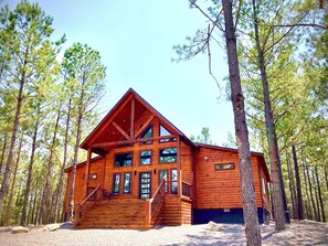 A log cabin with a staircase leading to the entrance, surrounded by trees.
