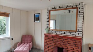 Um quarto com sofá rosa, lareira com fachada de tijolos, espelho grande e janela com persianas.