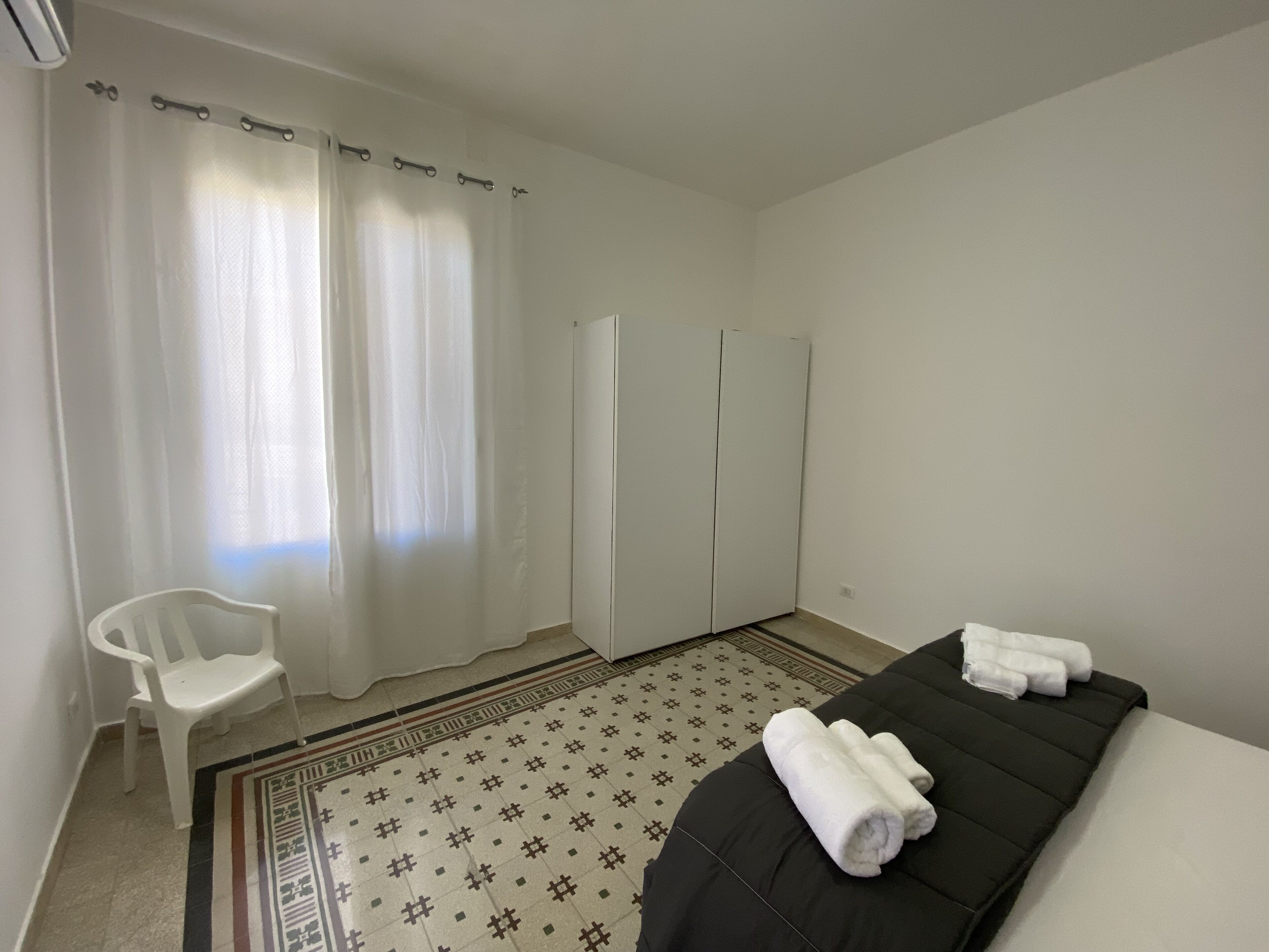 Hotellihuone, jossa on sänky, tuoli, vaatekaappi ja kuviollinen matto.