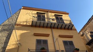 Un bâtiment à la façade jaune, dot é de deux fenêtres avec volets et d’un balcon orné d’une balustrade en fer forgé.
