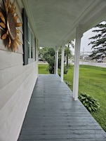 A covered porch with a wooden floor, white columns, and a sunflower decoration on the wall.
