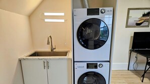 A compact laundry room with two stacked front-loading washing machines, a sink, and a small cabinet. - Sunflower Guest Suites (Summerside)