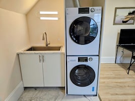 A compact laundry room with two stacked front-loading washing machines, a sink, and a small cabinet.