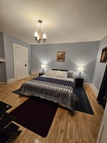 A bedroom with a bed, two bedside tables, a chandelier, a door, and a framed picture on the wall.
