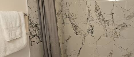 A bathroom with a bathtub, a shower curtain, and marble-patterned walls.