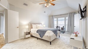 Ein Schlafzimmer mit Bett, Nachttisch, Lampe, Schreibtisch, Stuhl und Deckenventilator.